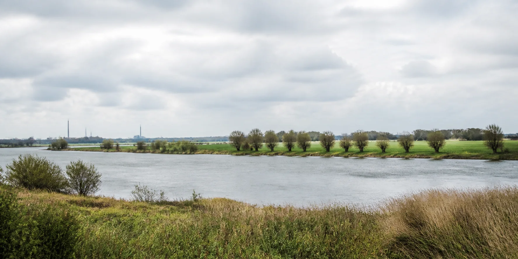Rhein, Felder und zurückhaltende Industrie am Horizont einer weiten Flusslandschaft